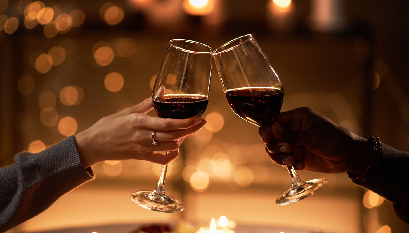 Close up of two people clinking wine glasses at dinner table