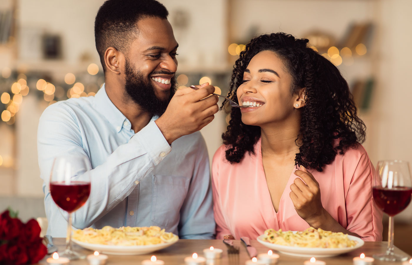 Smiling man feeding his date pasta during romantic dinner at home