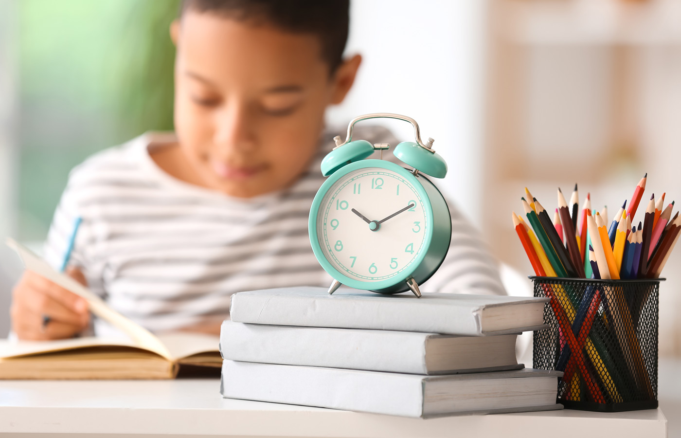 Alarm clock with books and pen cup on table of little boy doing lessons at home, closeup