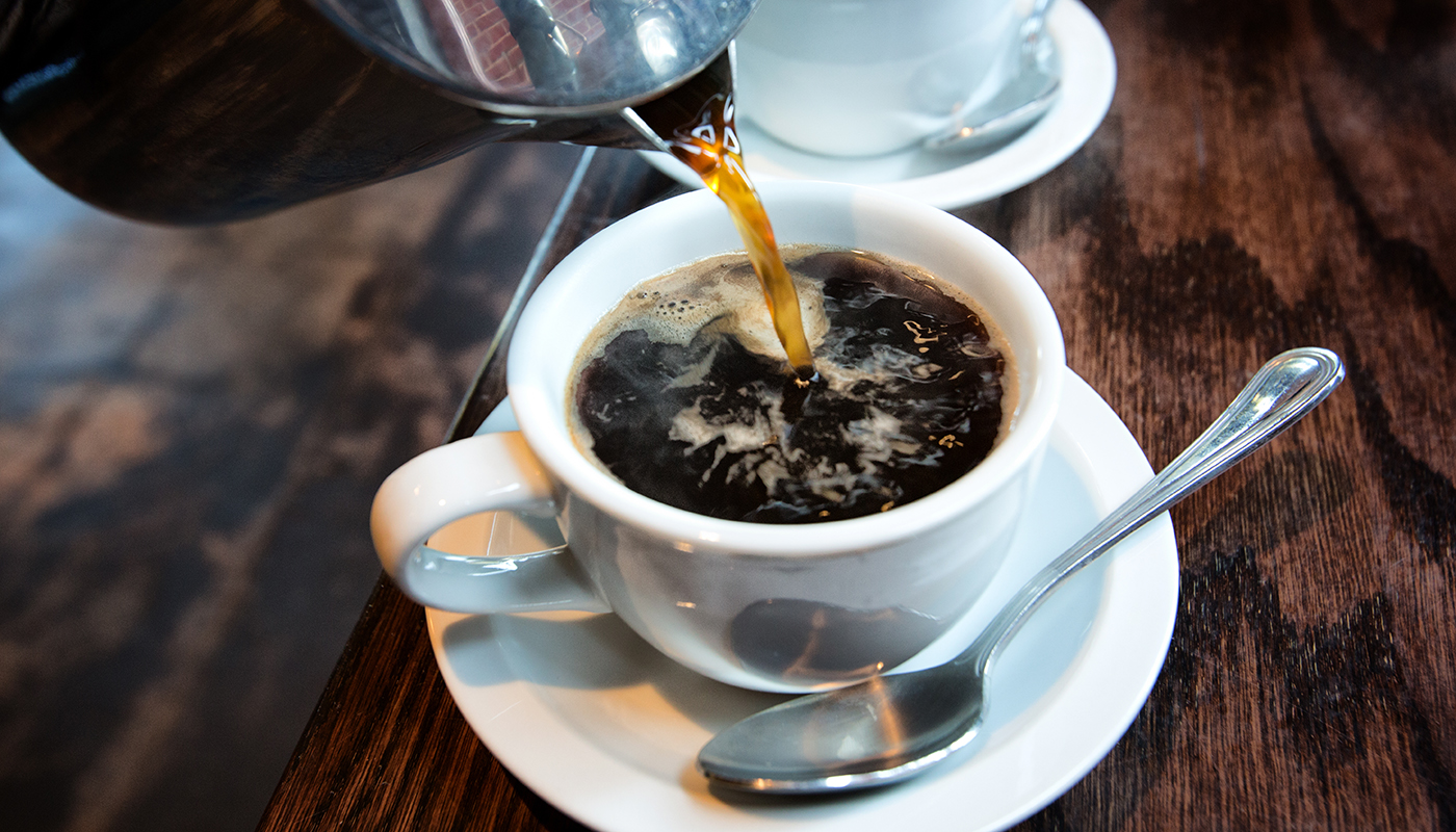Fresh hot coffee being poured into a cup with a saucer and spoon