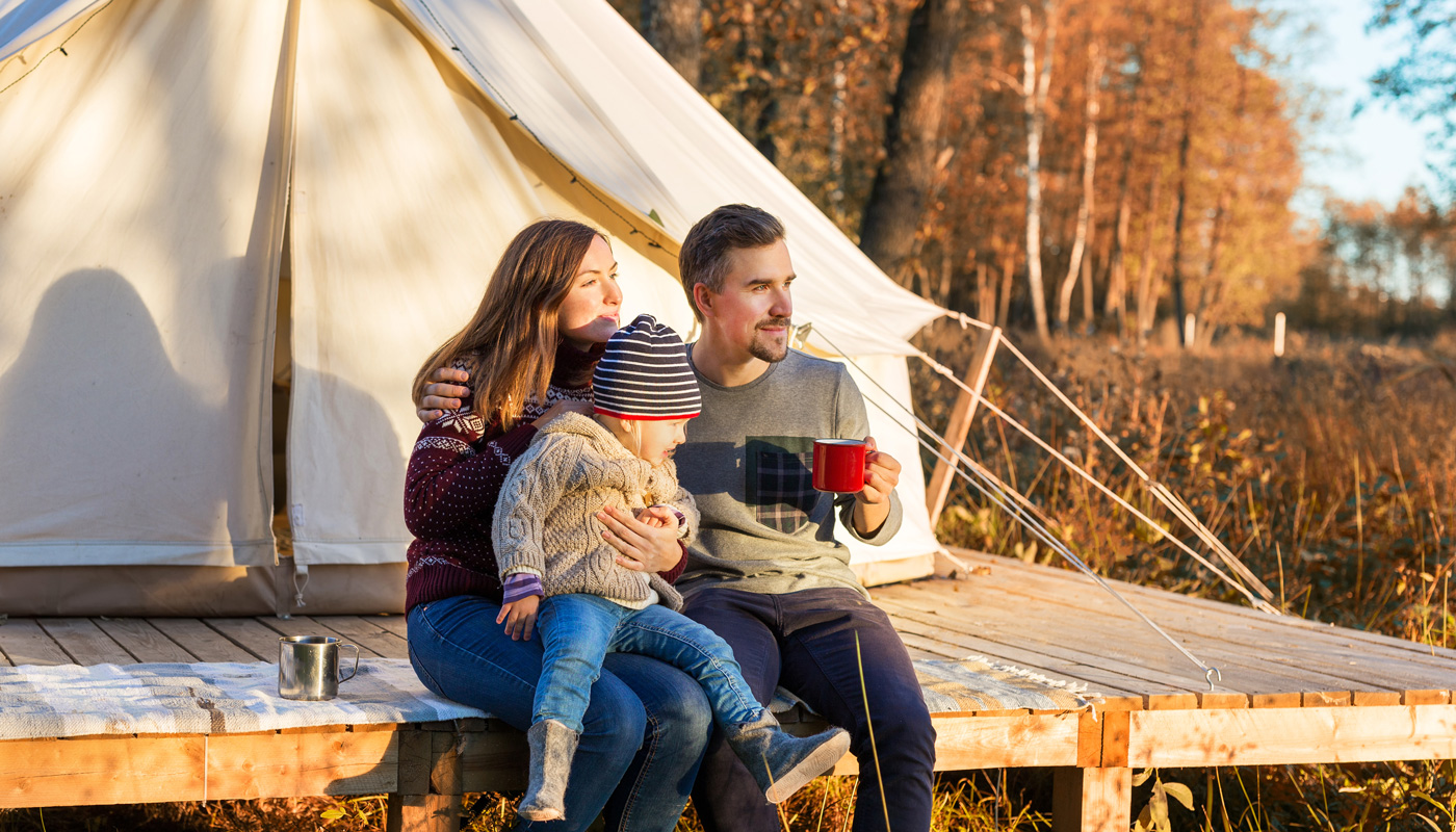 Happy family drinking coffee while sitting near canvas bell tent in a forest
