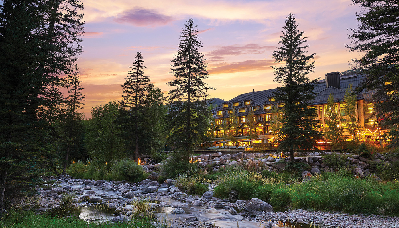 View of Grand Hyatt Vail at dusk with trees and a stream in foreground