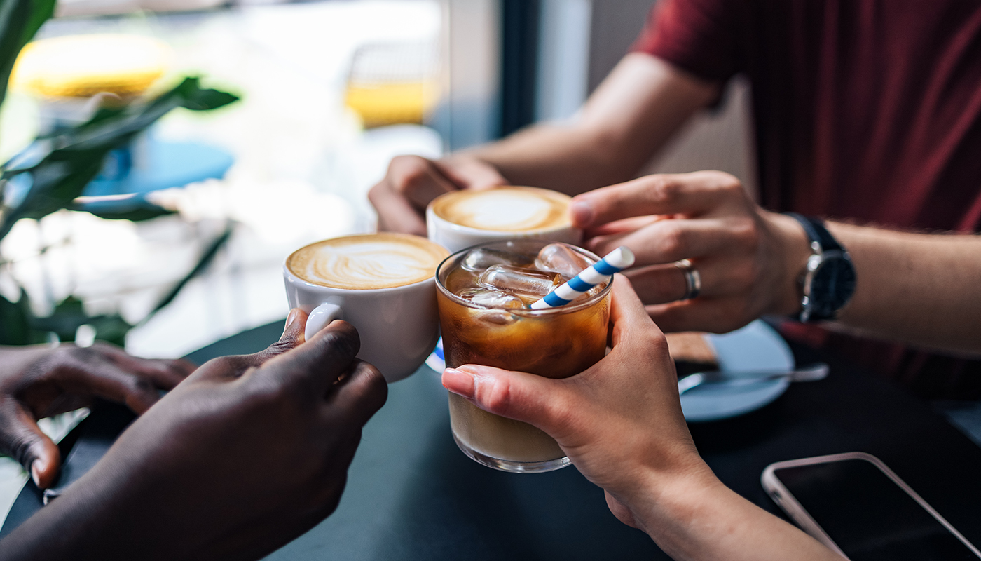 Close up of friends sitting at table together and holding various coffee beverages