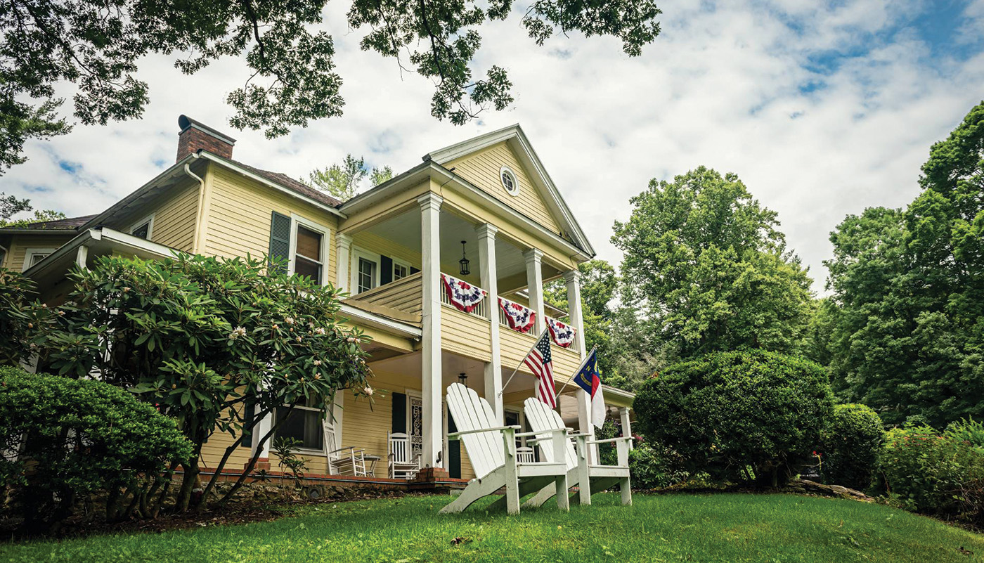Exterior view of yellow house with flags on porch and Adirondack chairs in foreground