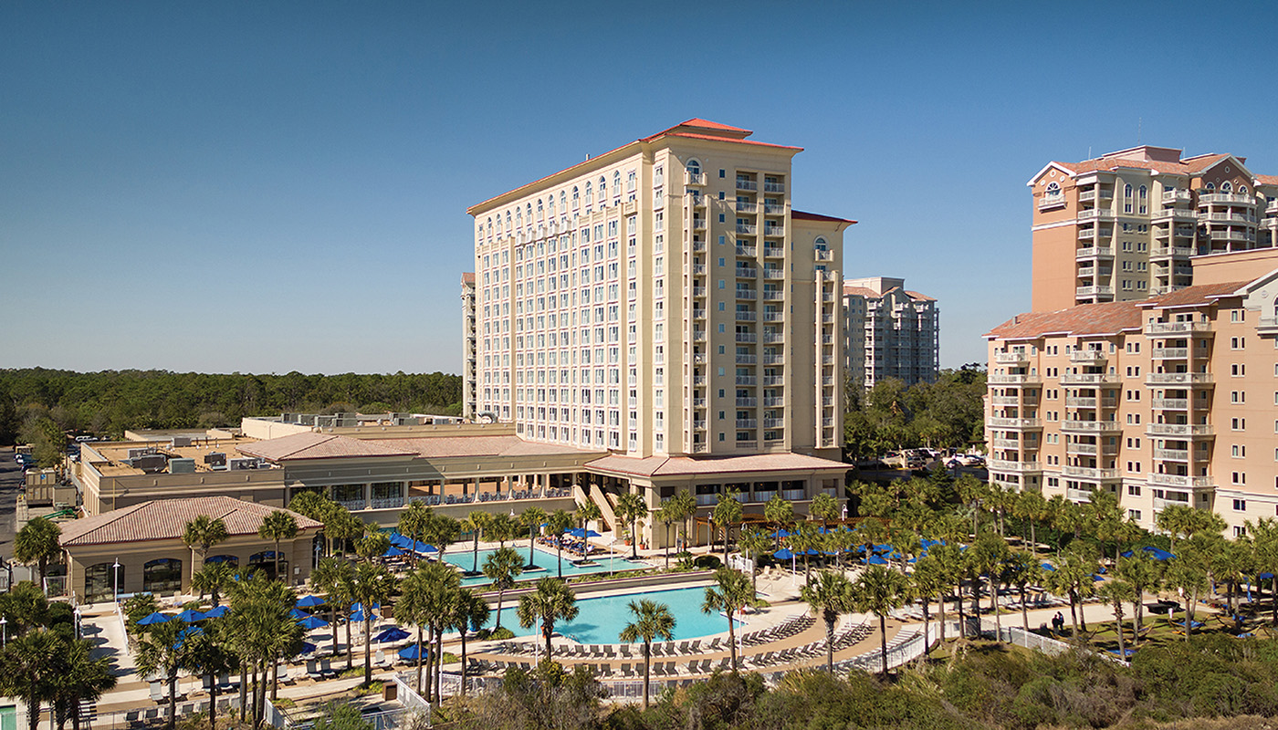 Exterior of high rise hotel with pool and palm trees in foreground