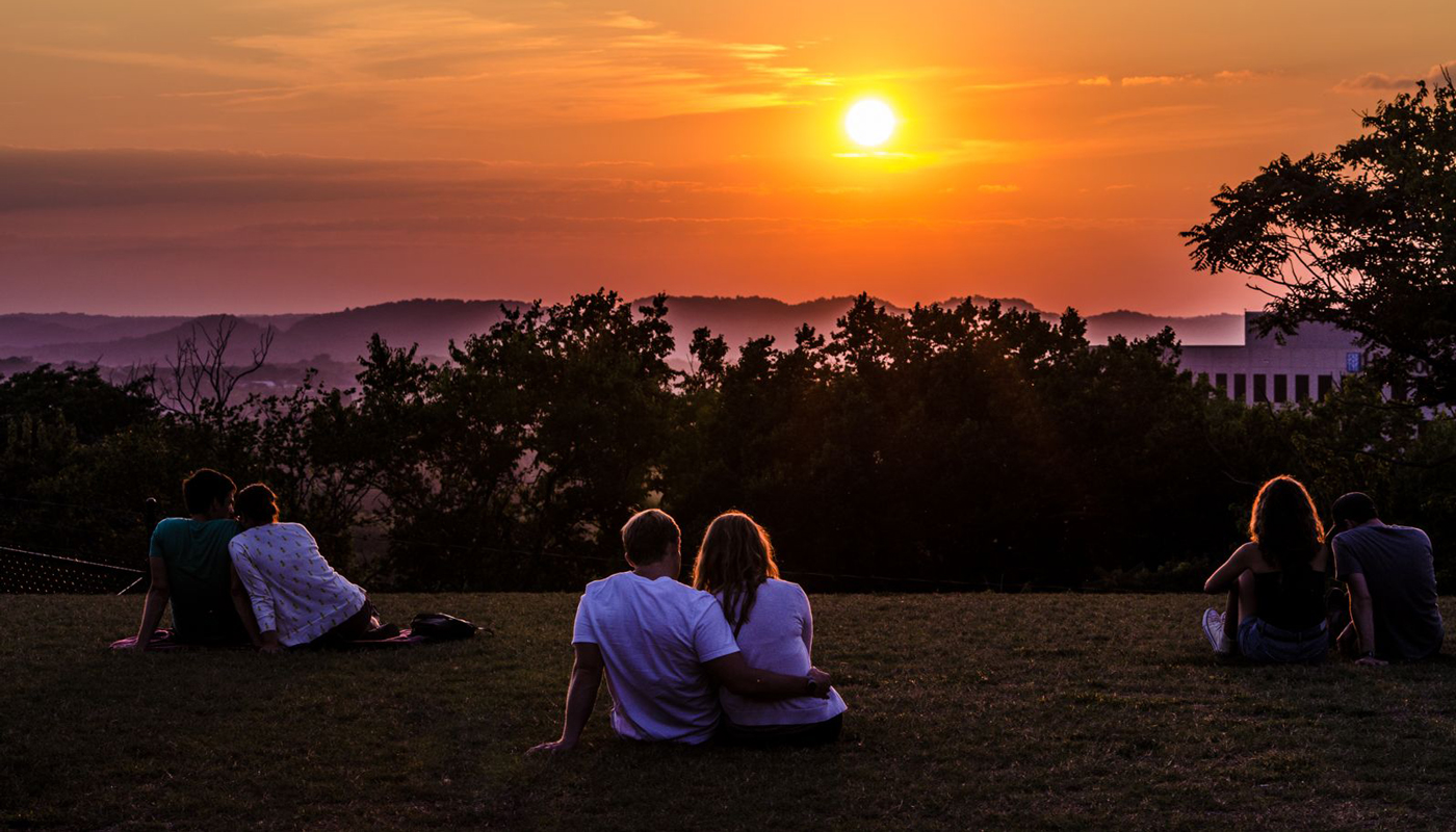 Couple sitting on a grassy area watching the sunset.