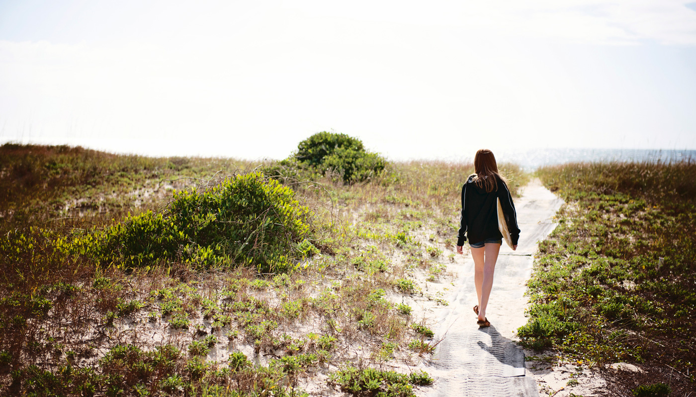 A woman walking down a sandy beach path toward the water in Florida.