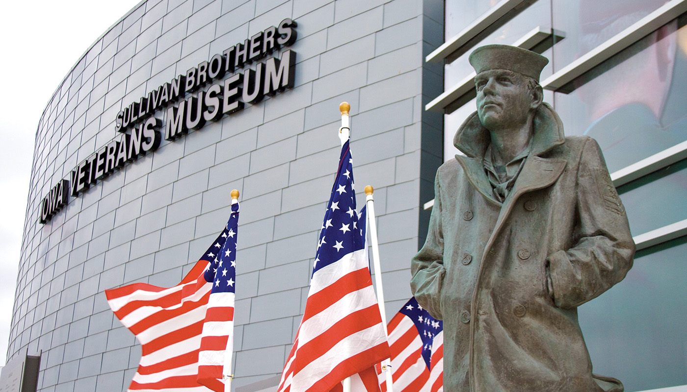 Exterior view of veterans museum with statue of soldier and American flags in foreground
