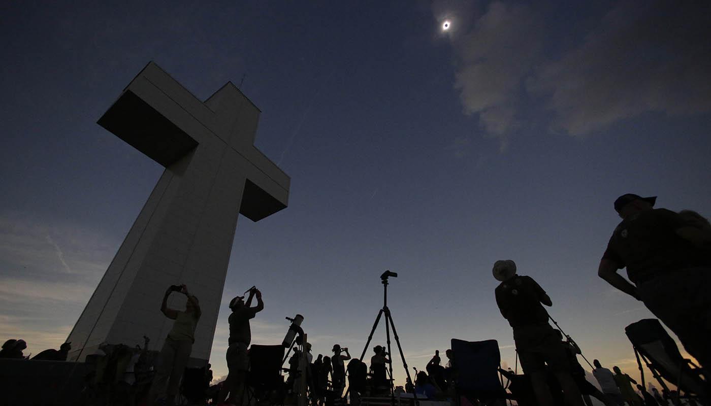 Onlookers gather under a large cross structure to observe an eclipse.