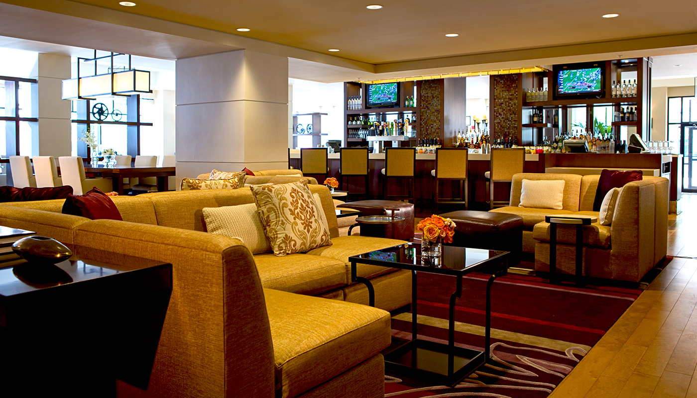 A hotel lobby with burgundy rugs, mustard couches and a bar.