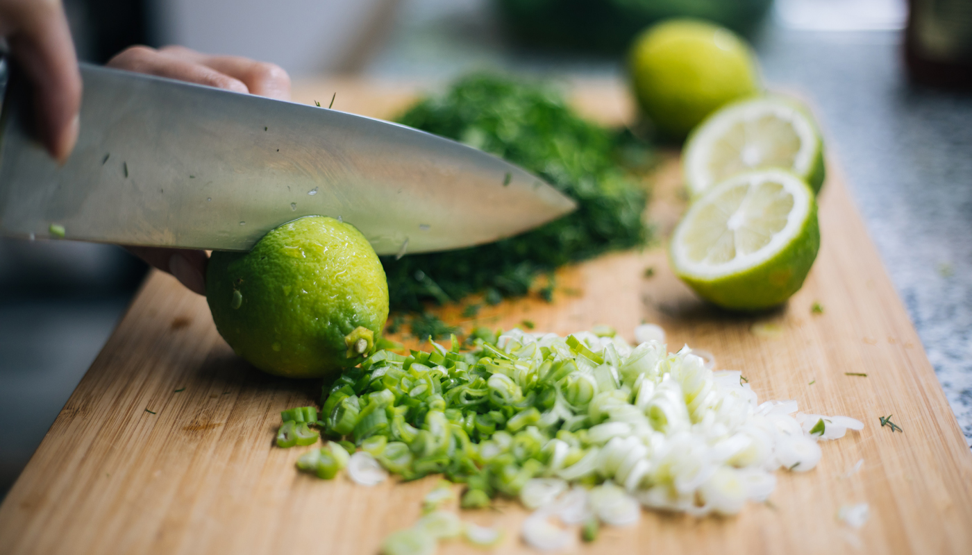 Closeup of hands using a chef’s knife to cut limes on a wood cutting board