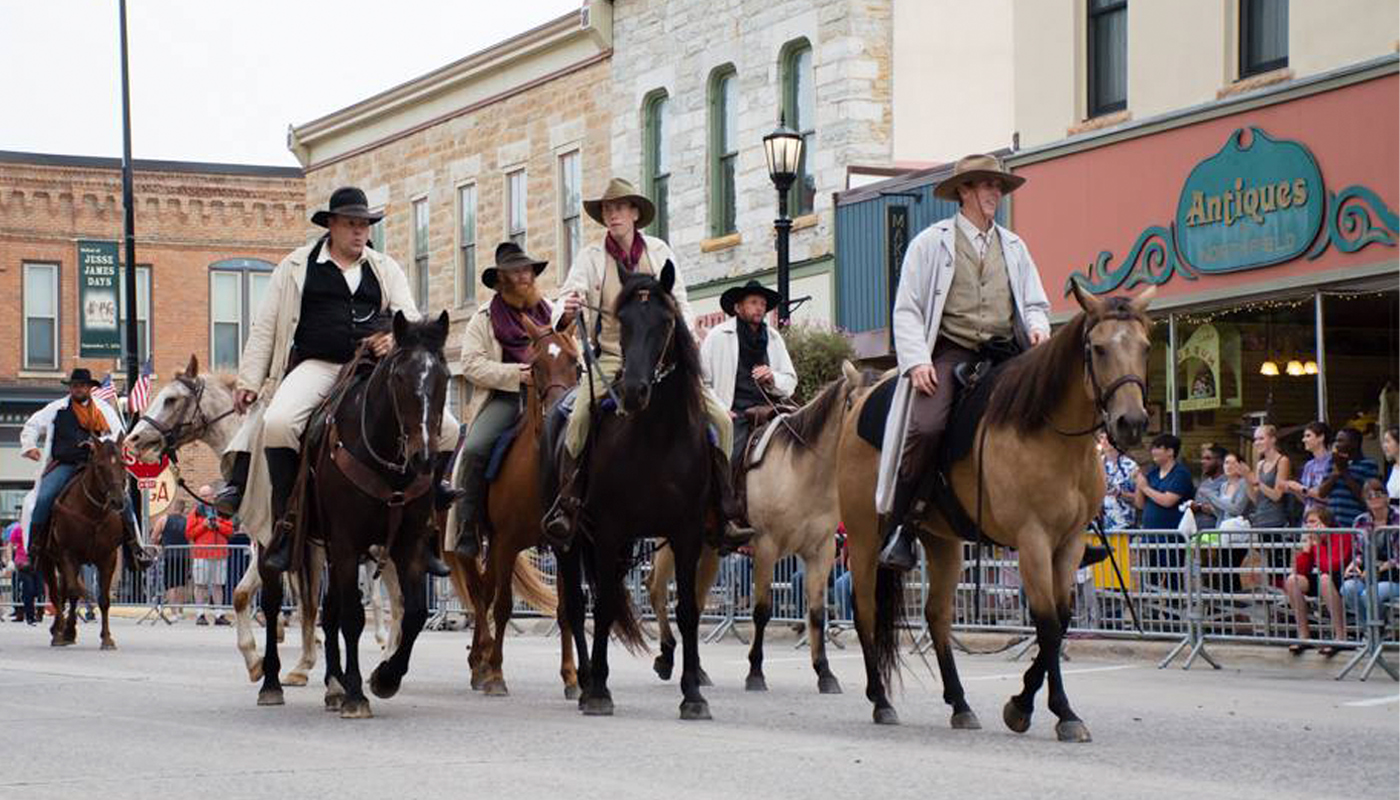 Re-enactors ride horses down the streets of Northfield with spectators on right