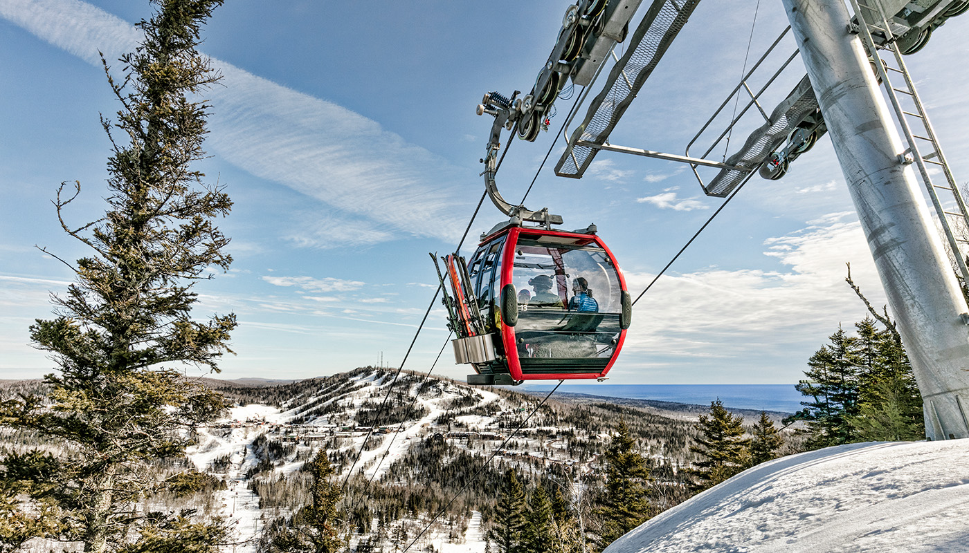 Gondola taking passengers up a snowy mountain with large pine trees on either side