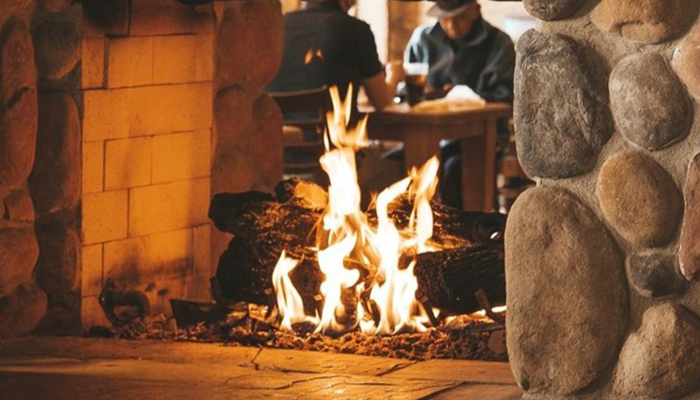 A double-sided log fireplace with stone surround  in a restaurant.
