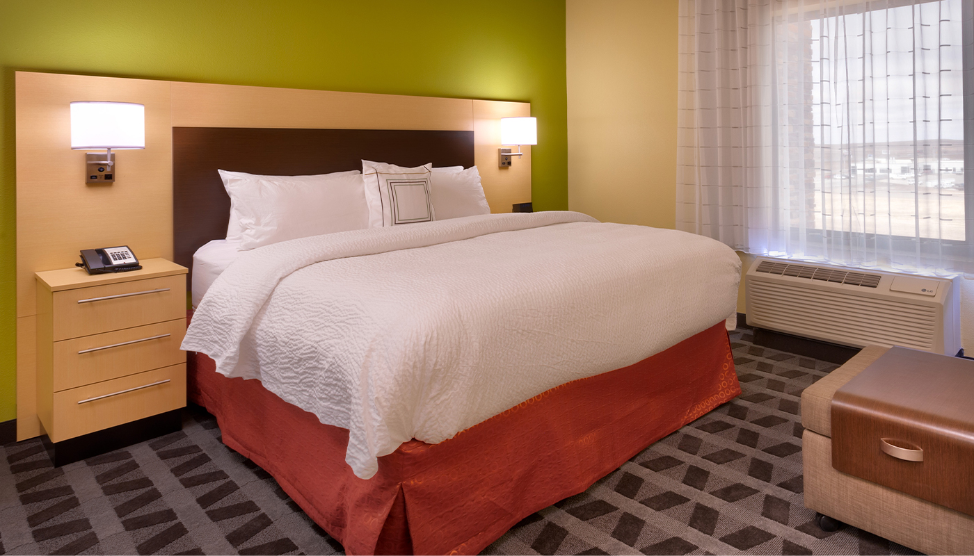 A large bed with a wood headboard and lit sconces in a hotel room.