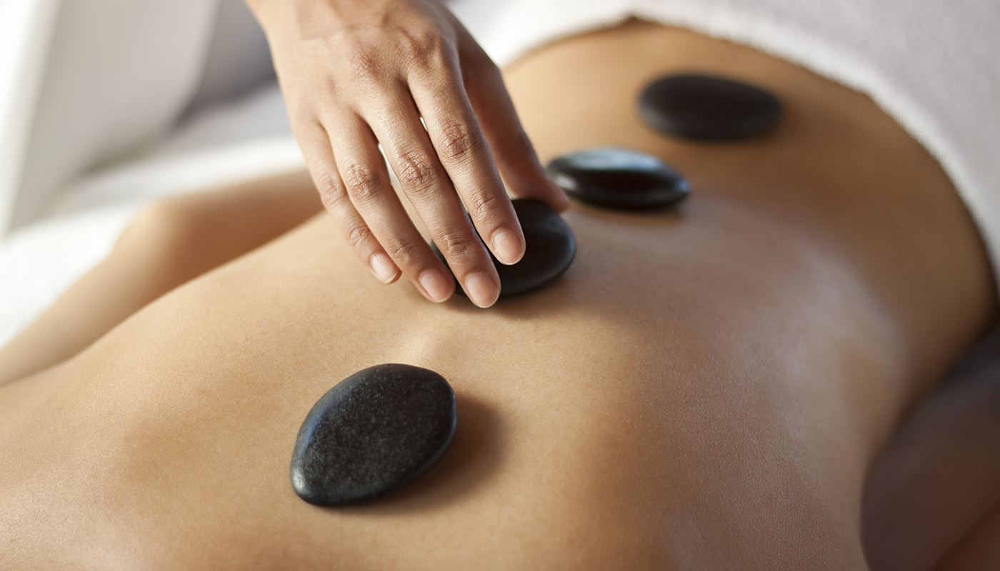 Closeup of hands placing hot stones on person's lower back 