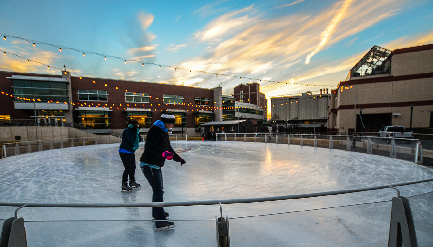 Two people ice skating in the evening at University of Nebraska Medical Center's outdoor ice rink with the medical center in the background