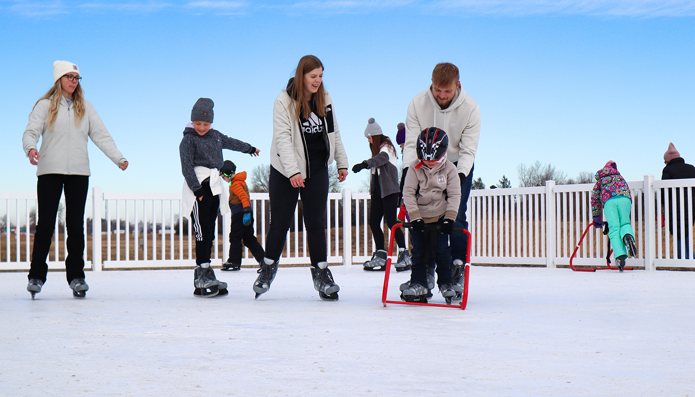 Various adults and children ice skate outdoors at the Glaciarium at Grand Island’s Stuhr Museum. A white fence is behind the ice skaters