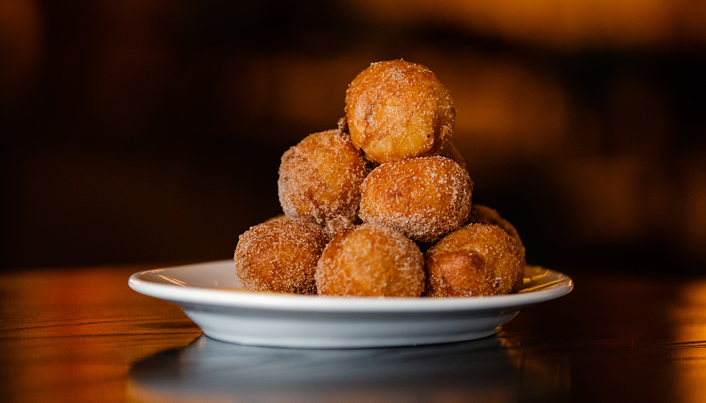 A stack of Portuguese cinnamon-sugar doughnuts in the shape of a pyramid on a dessert plate.