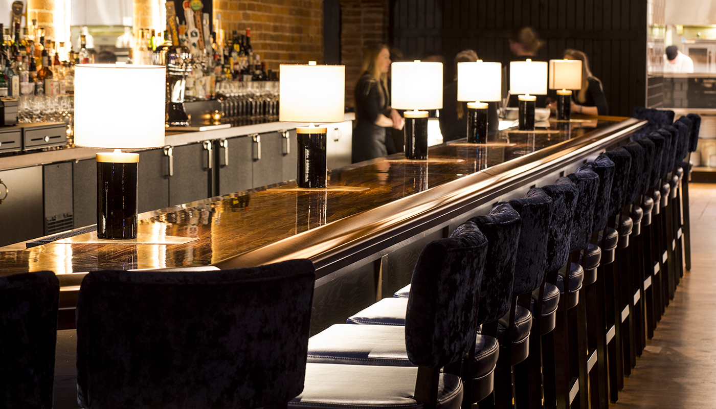 A bar lit with a row of small lamps.. Barstools are on the right.