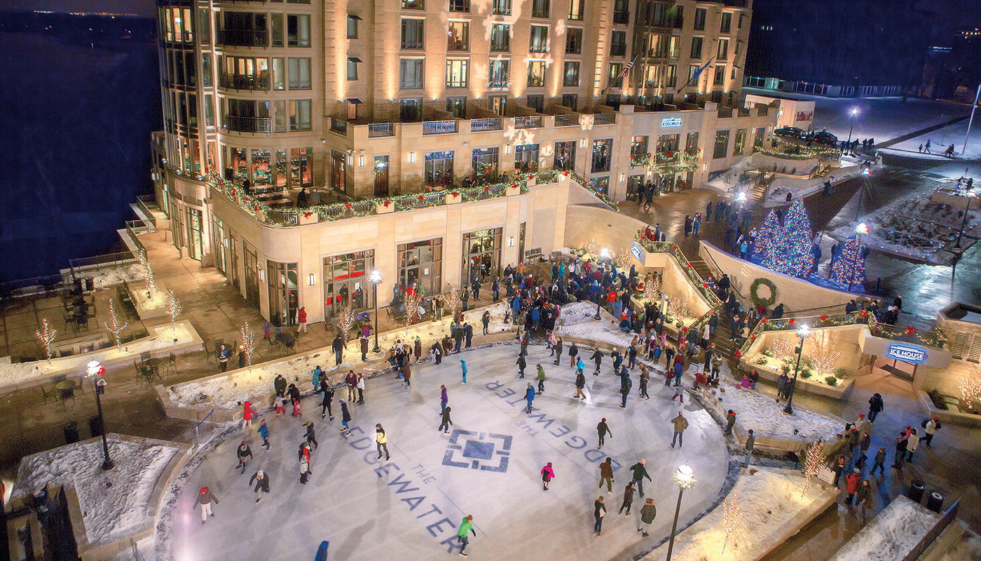 Aerial view of various ice skaters on an ice rink at night with illuminated lights