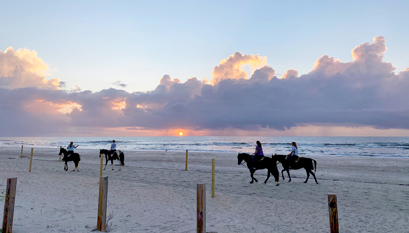 Various people horseback riding on Amelia Island beach at dusk