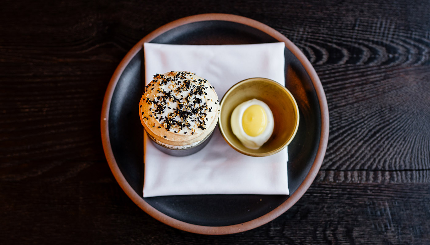Overhead view of a lemon souffle topped with meringue and black sesame seeds on a black plate