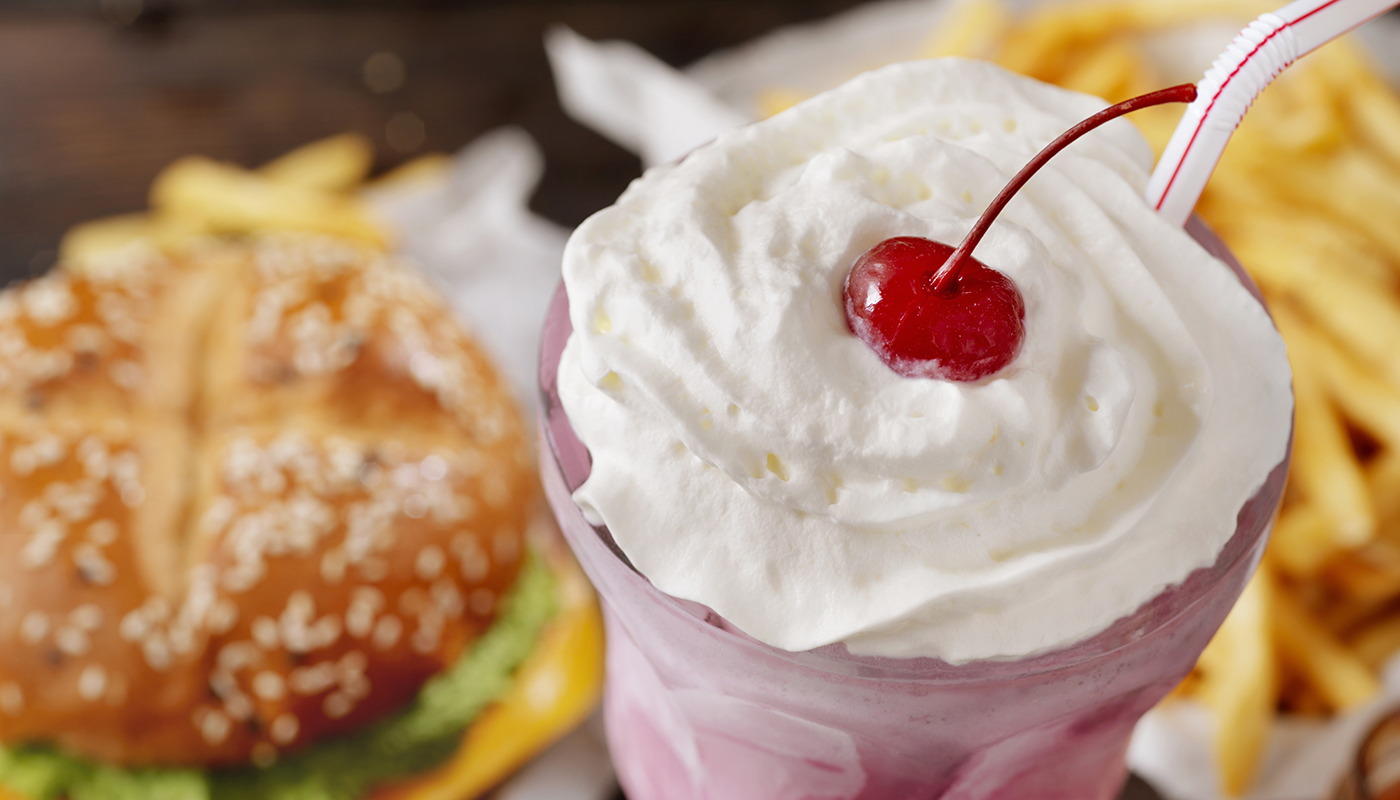 Strawberry milkshake, topped with whipped cream and a cherry,  and a burger and french fries
