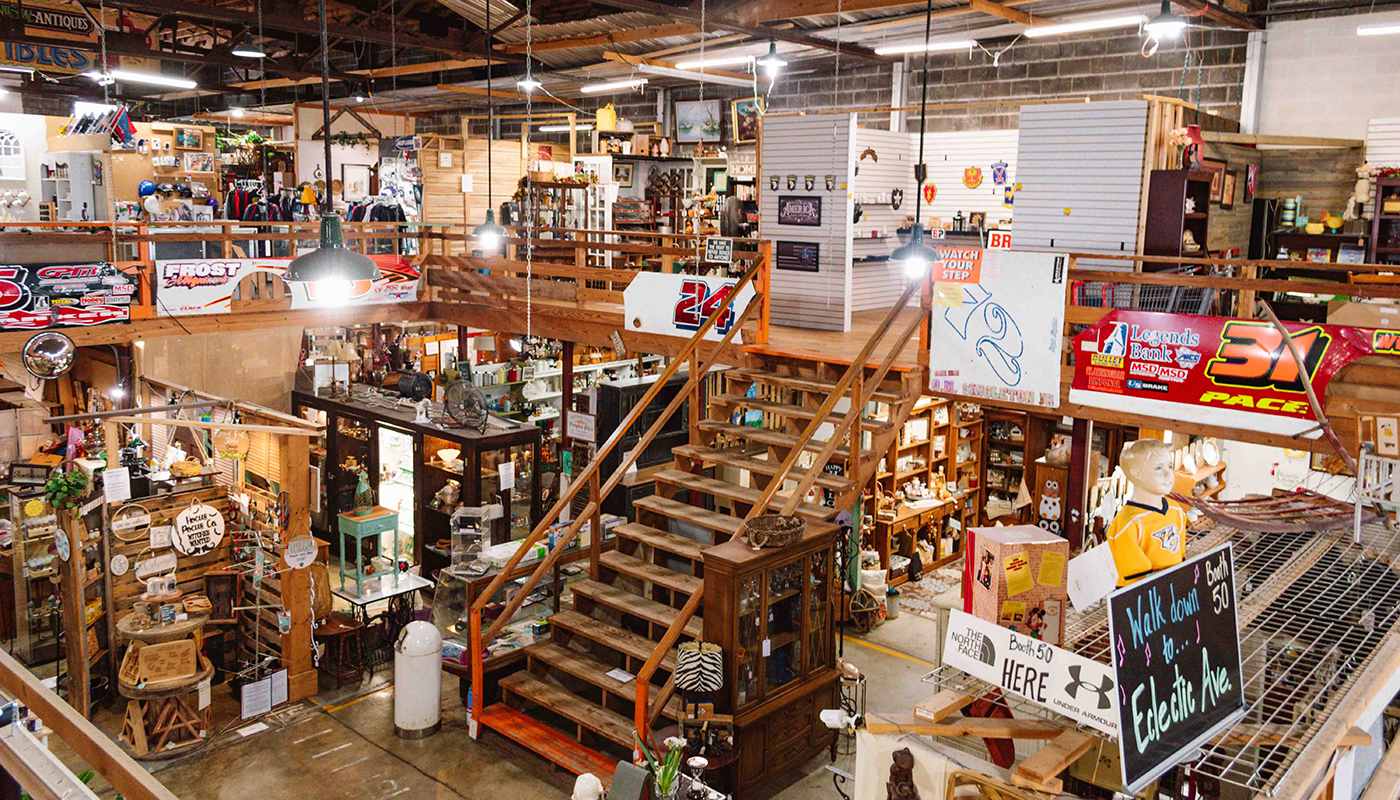 The interior of a two-level vintage market, filled with signage, pottery, clothing and lamps.
