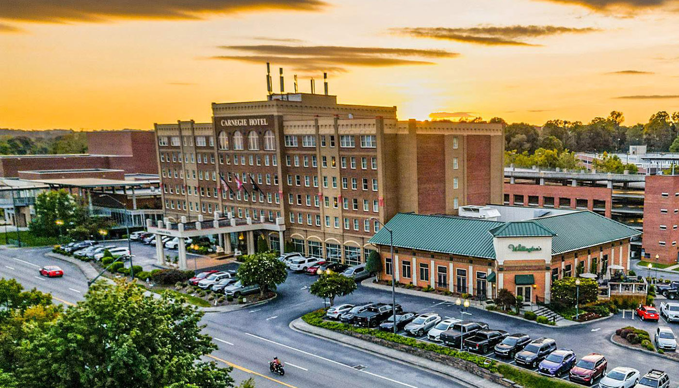 Aerial view of the brick Carnegie Hotel at sunset. A parking lot full of cars is in the foreground.