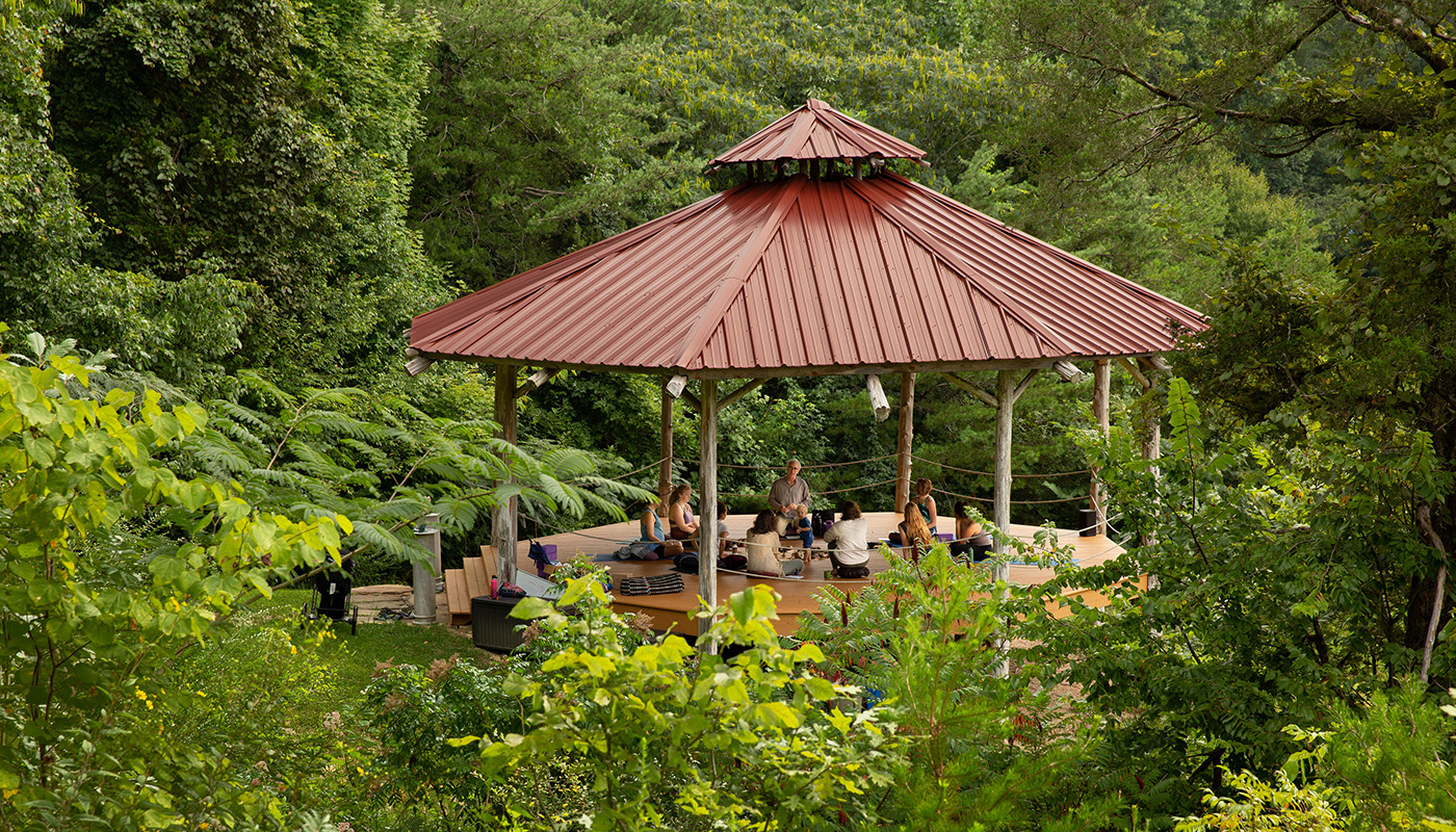 Patrons practicing open-air yoga in a shala outside, surrounded by trees