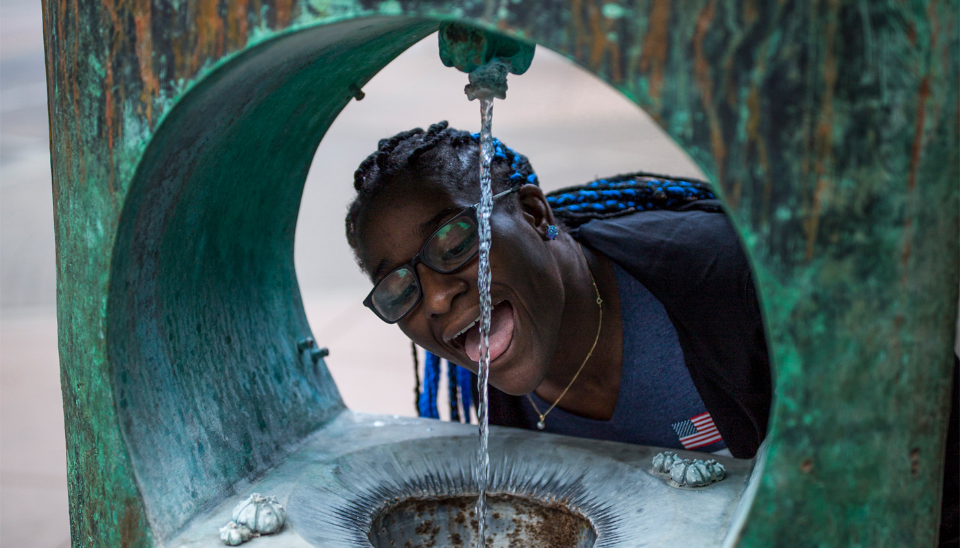 A young woman drinks from a water fountain supplied by a natural spring.