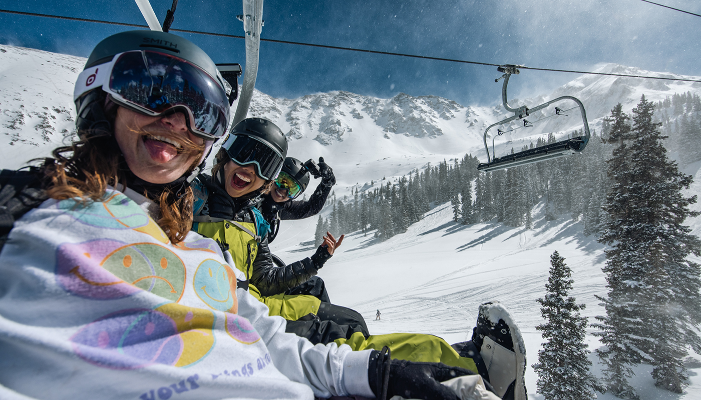 Three skiers taking a selfie while riding a ski lift on a snowy mountain
