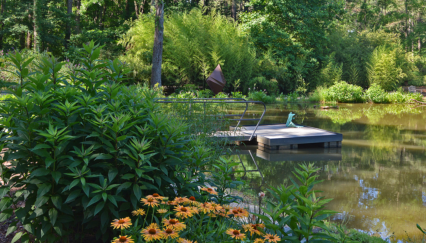 A small dock on a pond surrounded by dense greenery and blooming flowers.