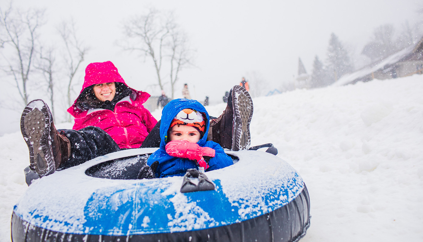 Adult and child inner tubing on a snowy hill