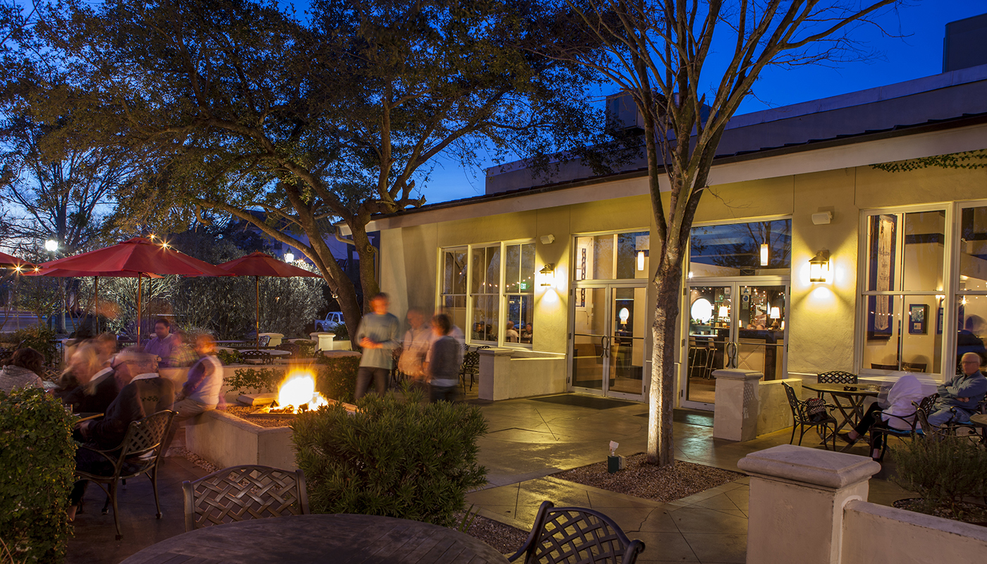 Patrons enjoying a fire pit in the outdoor dining area of a restaurant at night. 