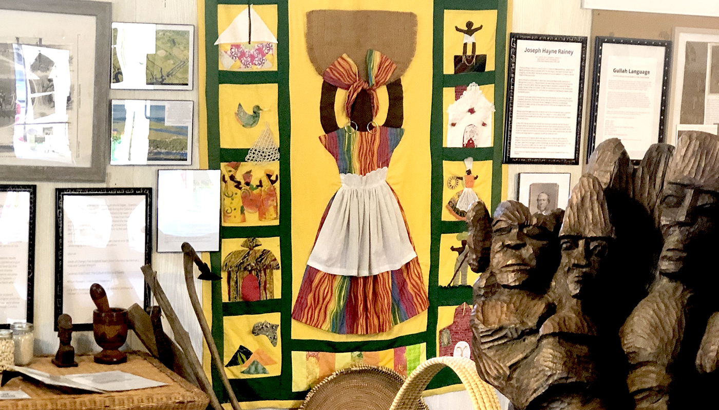 Traditional Gullah art of a woman in a colorful dress holding a basket overhead.