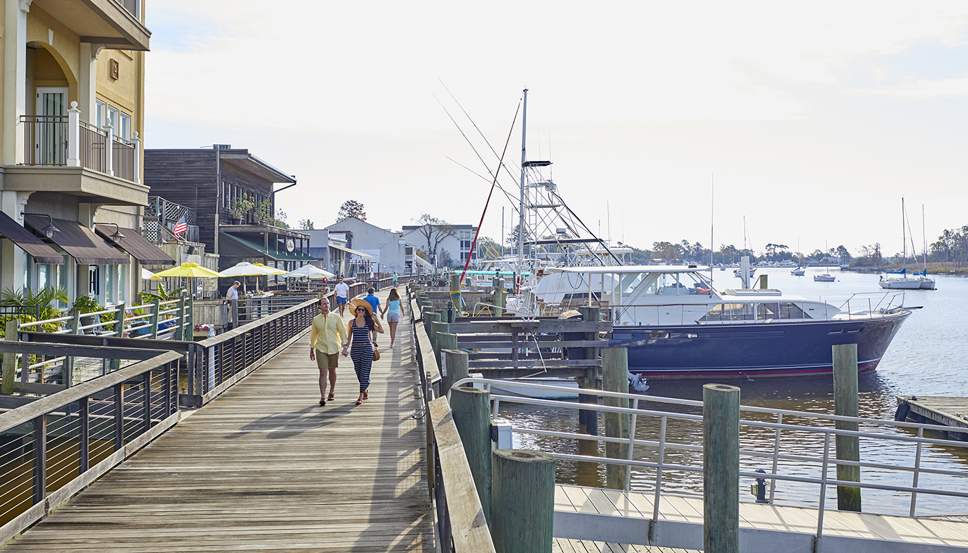 People walk on boardwalk lined with shops on the left and boats on the right.