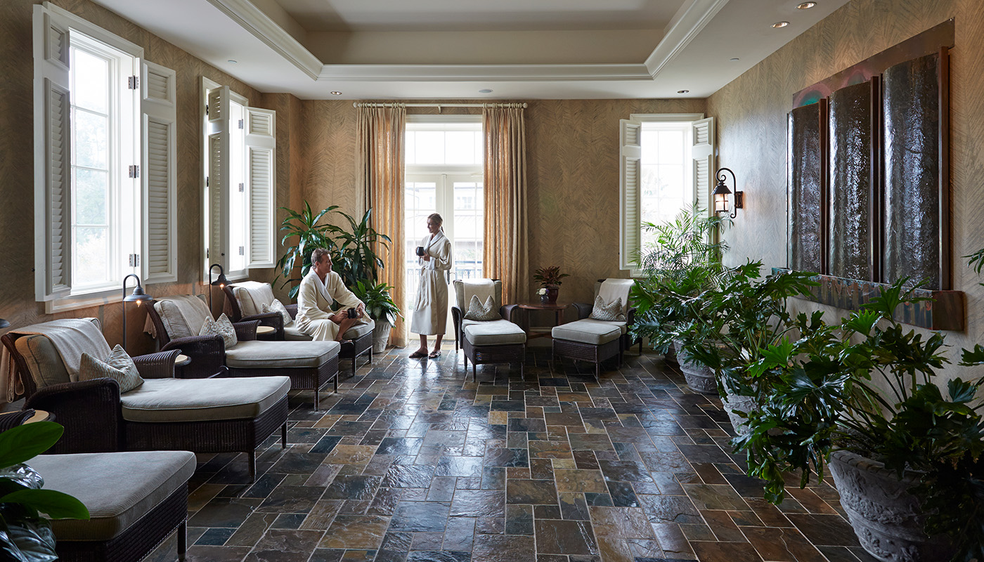A couple in robes relax in a large spa treatment room with tile floor