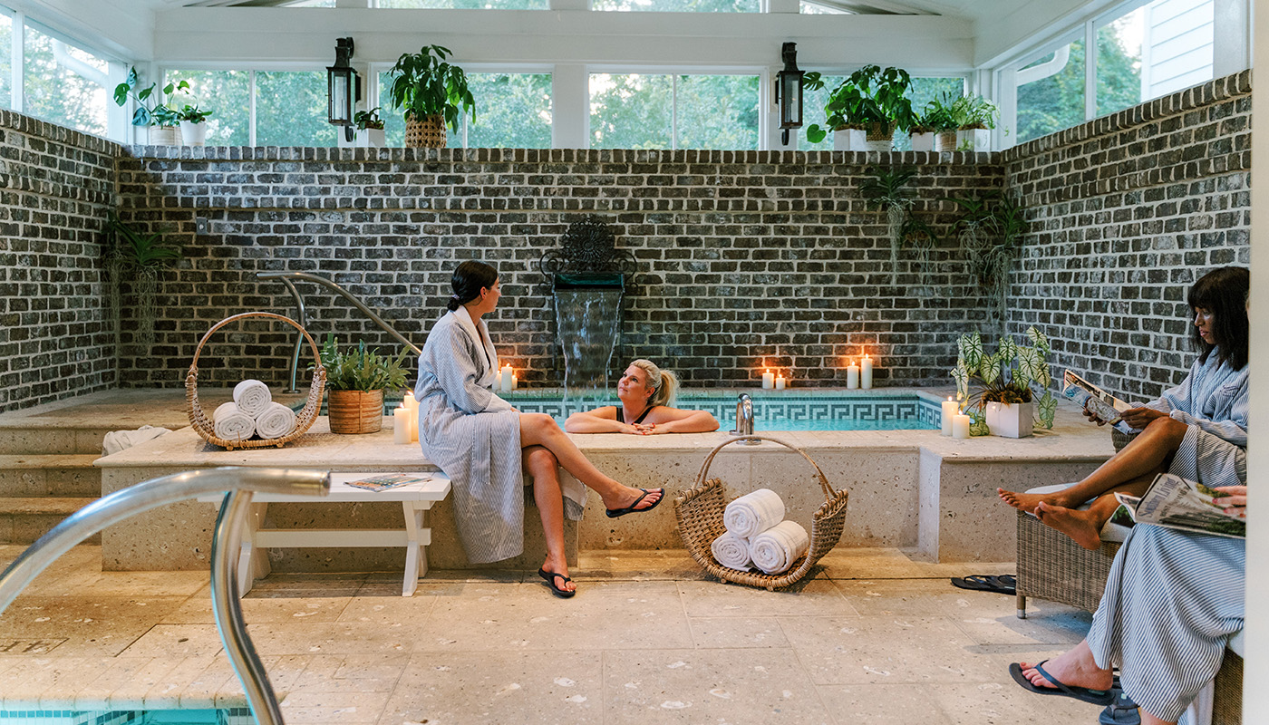 Women relax in an indoor soaking pool, surrounded by a brick wall