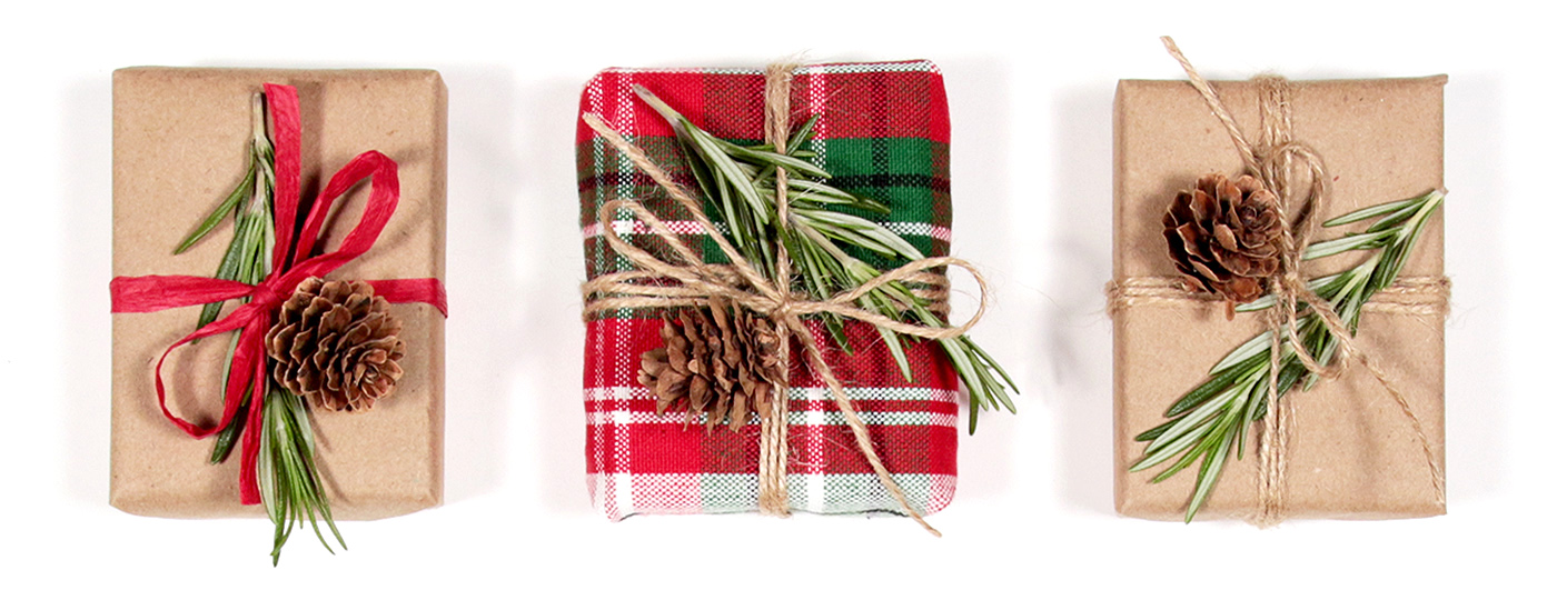 top view of presents wrapped in kraft paper and a dish towel, decorated with twine, rosemary and mini pine cones