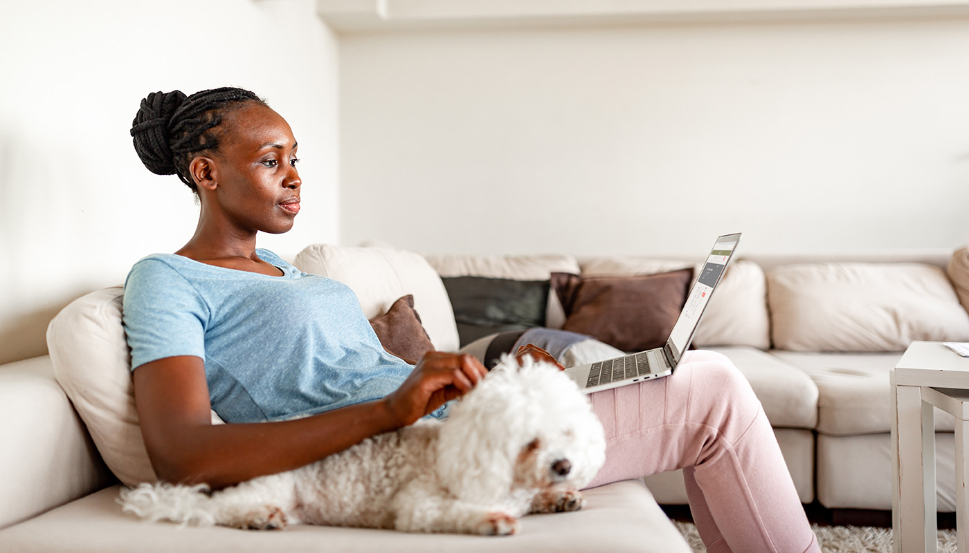 Woman sitting on sofa with dog, looking at laptop