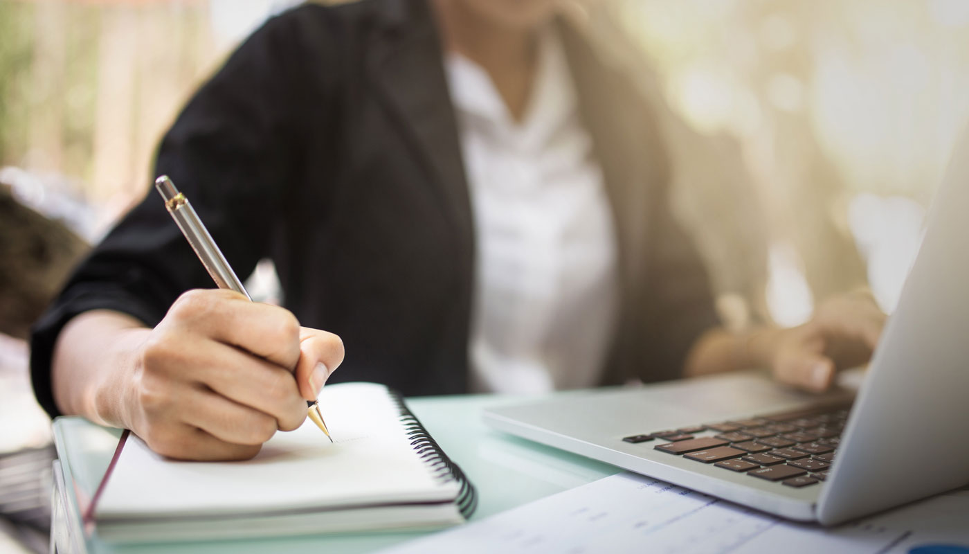 woman working on laptop and writing notes