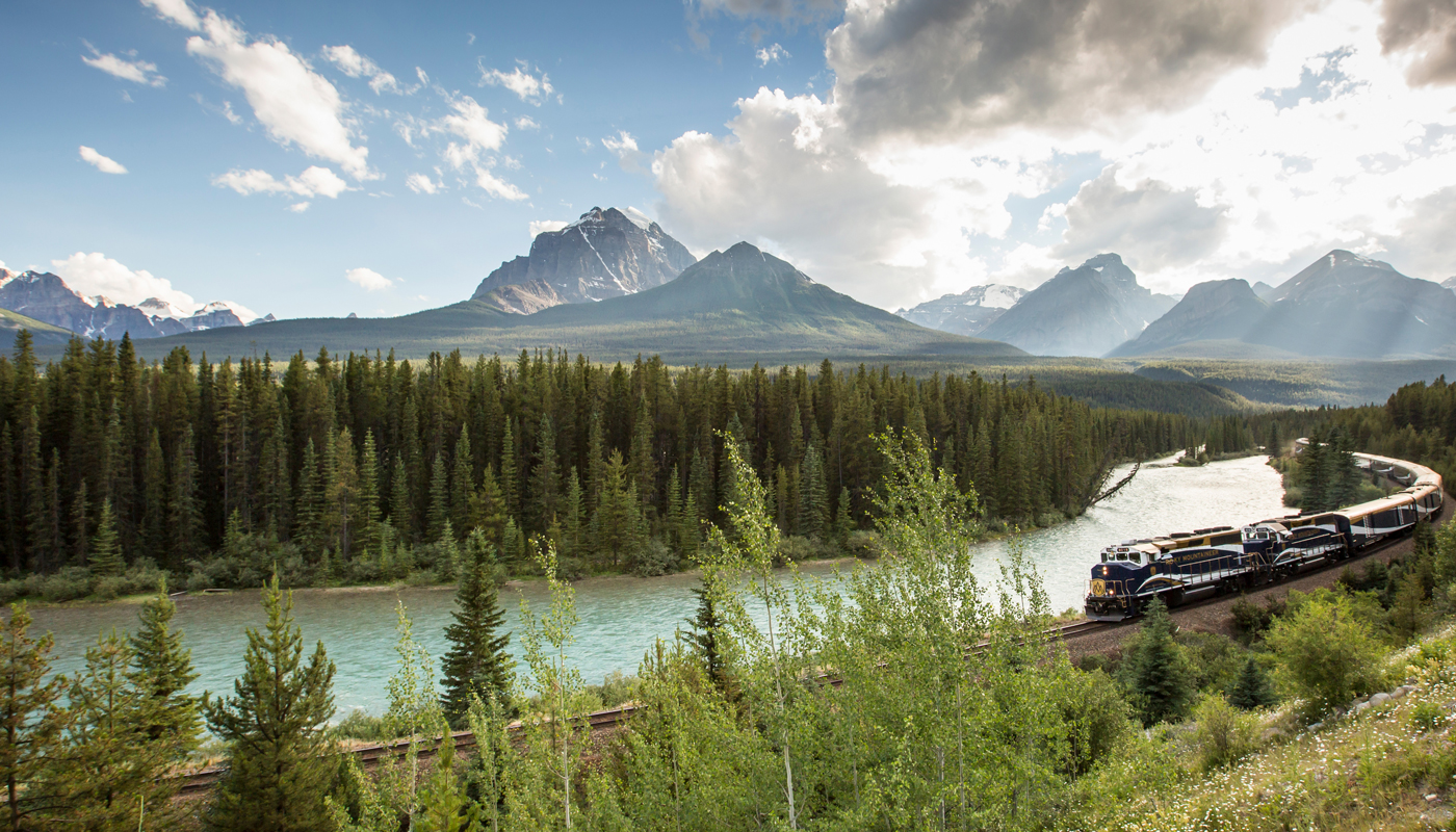 A view of the Alaska mountains with a river and a train in the foreground