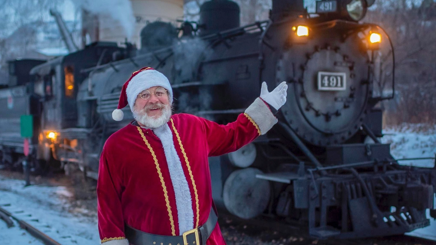 Santa Claus stands in front of THE POLAR EXPRESS™ at the Colorado Railroad Museum. 