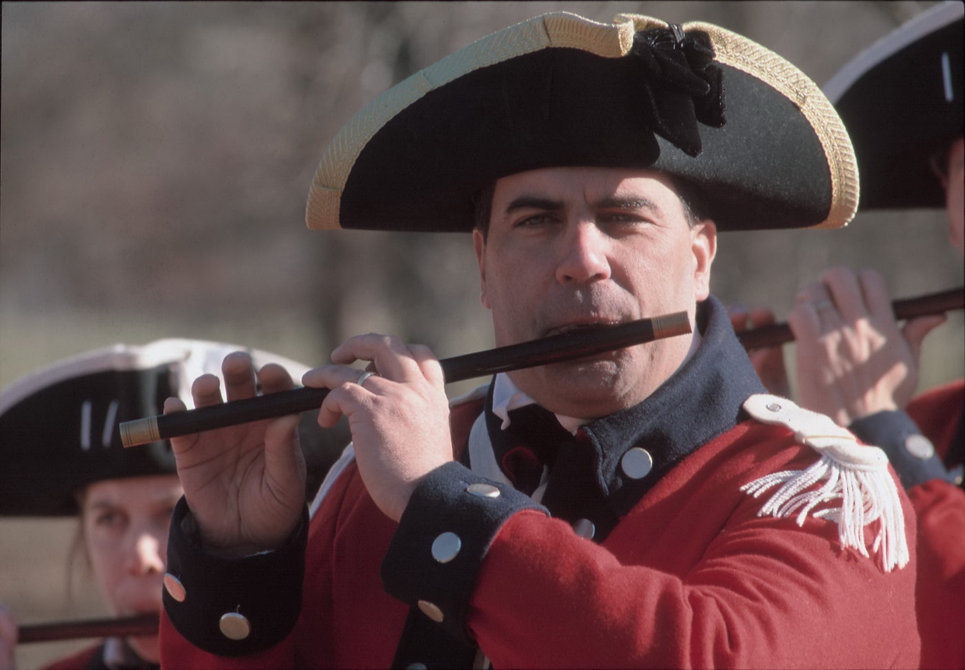 A man dressed in a Revolutionary War uniform playing a fife.