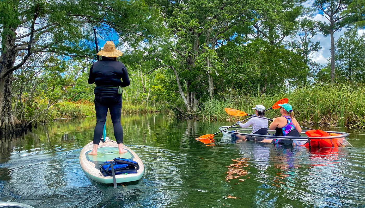 One person on a paddle board and two people in a kayak on the water.