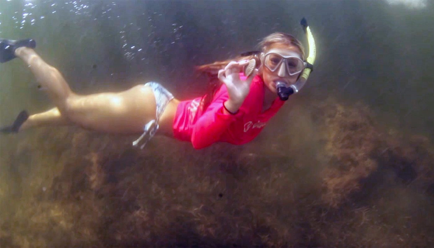 Young women underwater with a mask and snorkel holding a scallop in her hand.