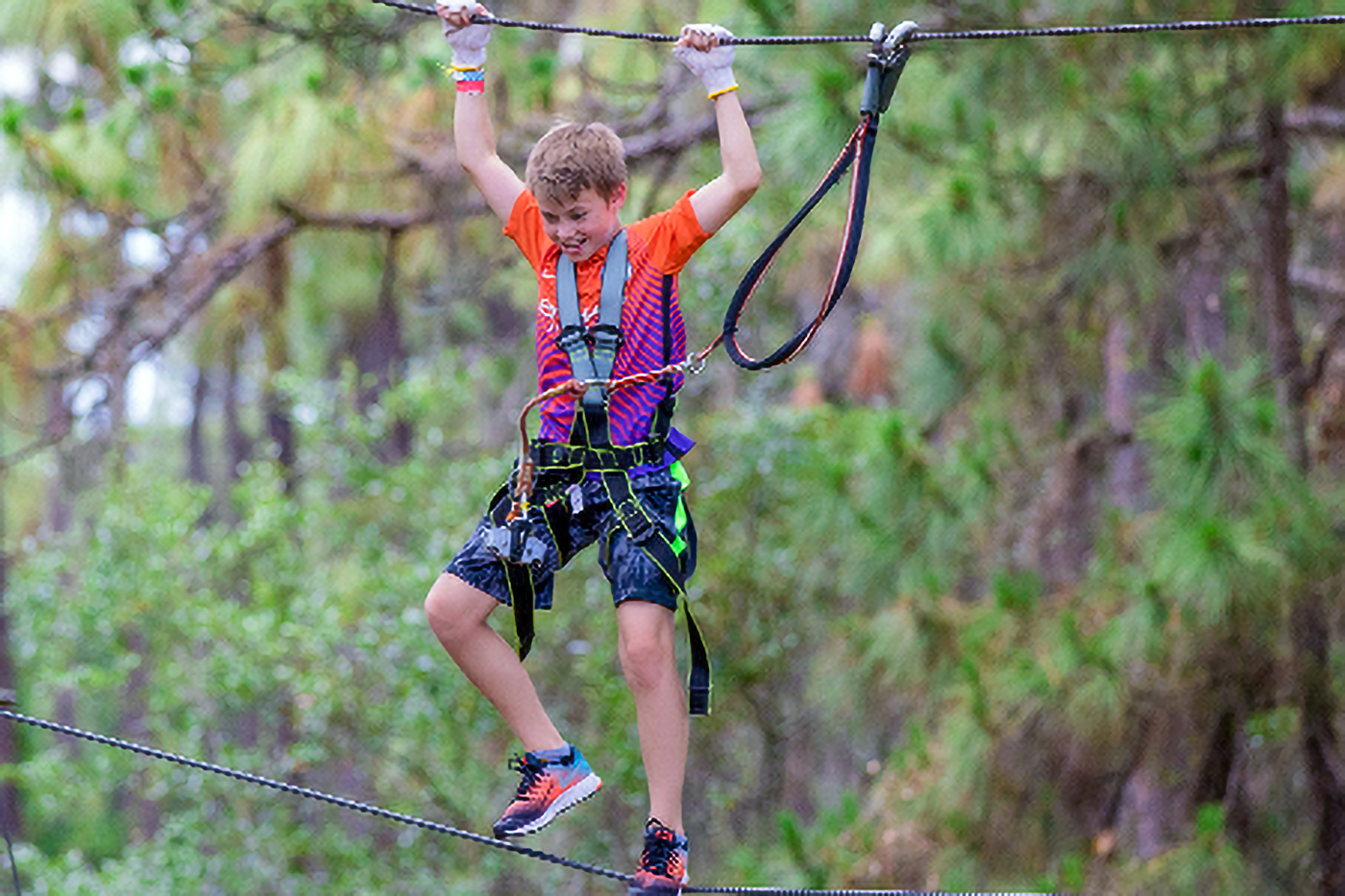 Boy wearing shorts and a t-shirt on a high ropes course.