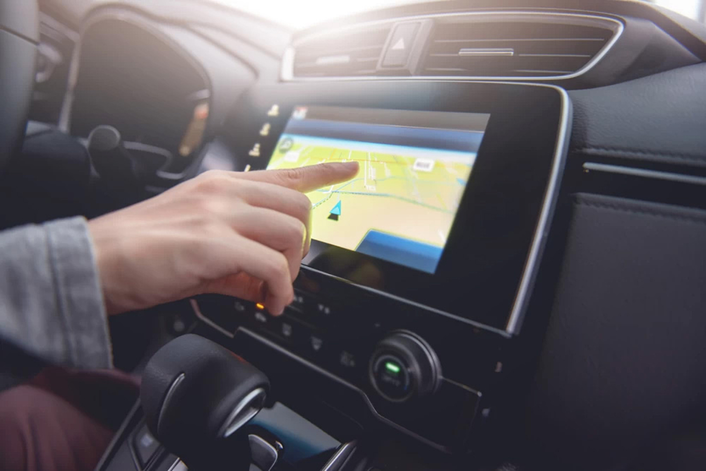 A person's hand with their pointer finger on the gps touch screen on the car dashboard.